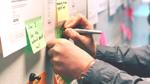 Person writing on a post-it note on a wall
